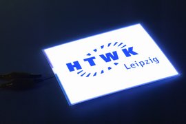Leuchtende LED-Tafel in abgedunkeltem Raum mit Logo der HTWK Leipzig.
